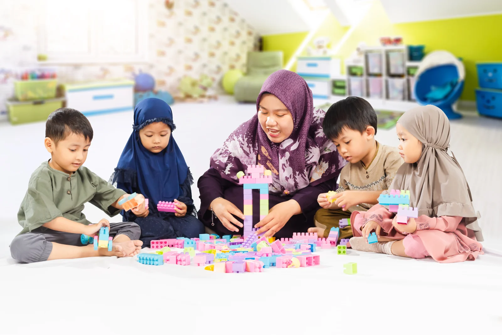 Guru dan empat anak tanpa seragam bermain balok warna-warni